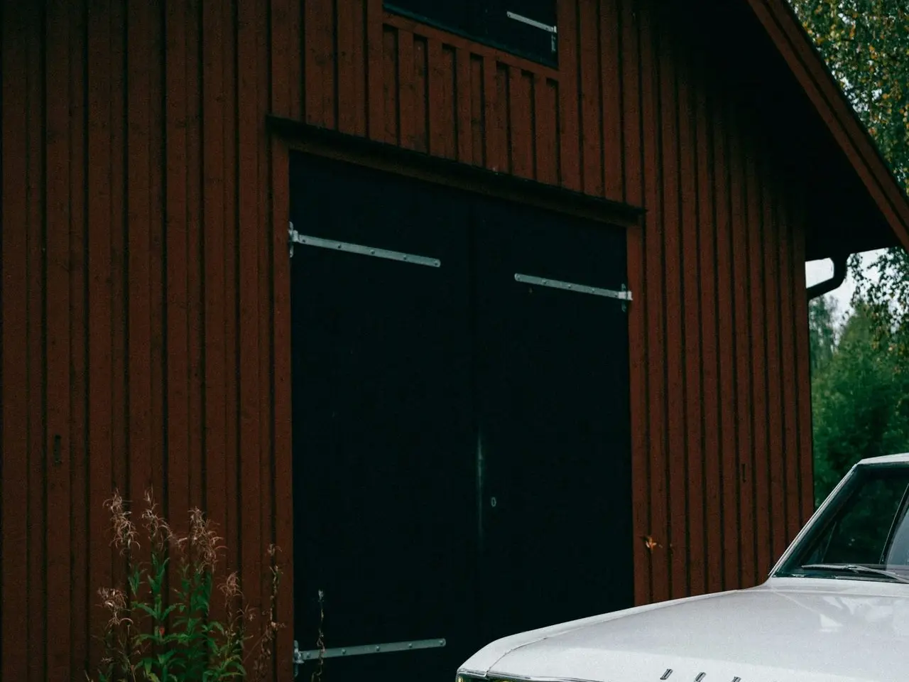 a white car parked in front of a red barn